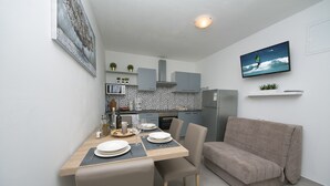 A compact kitchen with modern appliances, a dining area with a table set for four, and a sofa in a living area.