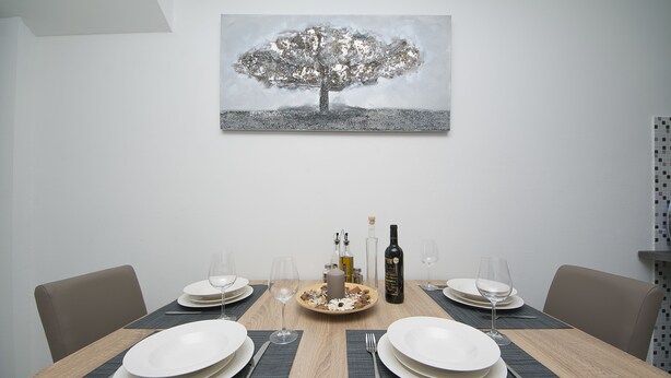 A dining table set for two with plates, cutlery, and glasses, a candle, and a bottle of wine.