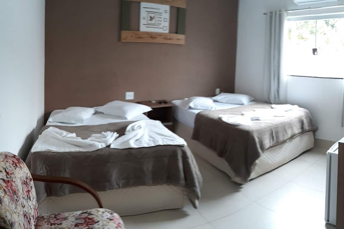 A hotel room with two beds, a chair, a desk, and a window.