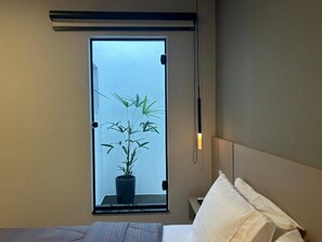 Un dormitorio con una cama, una ventana con vistas a una planta y una mesita de noche.