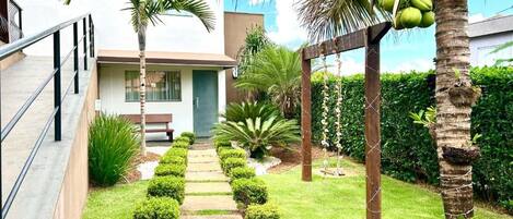 A modern outdoor area with a paved walkway, palm trees, and neatly trimmed bushes.