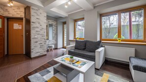 A modern living room with a sofa, coffee table, and a view of the outside through large windows. - RentPlanet - Apartament Krzeptówki (Zakopane)