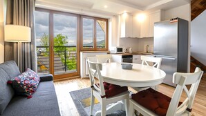 A modern kitchen with white cabinets, a stainless steel refrigerator, and a dining area with white chairs and a round table. - RentPlanet - Apartament Krzeptówki (Zakopane)