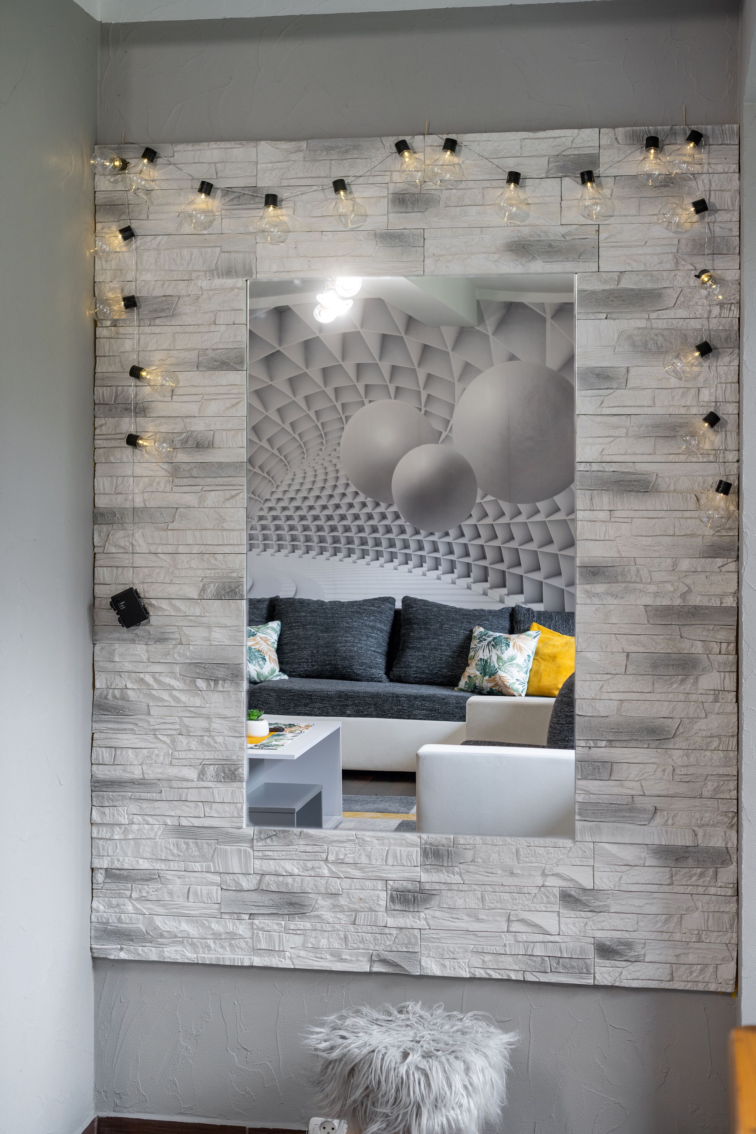 Una sala de estar moderna con pared de textura de piedra, un sofá con cojines y una lámpara decorativa.