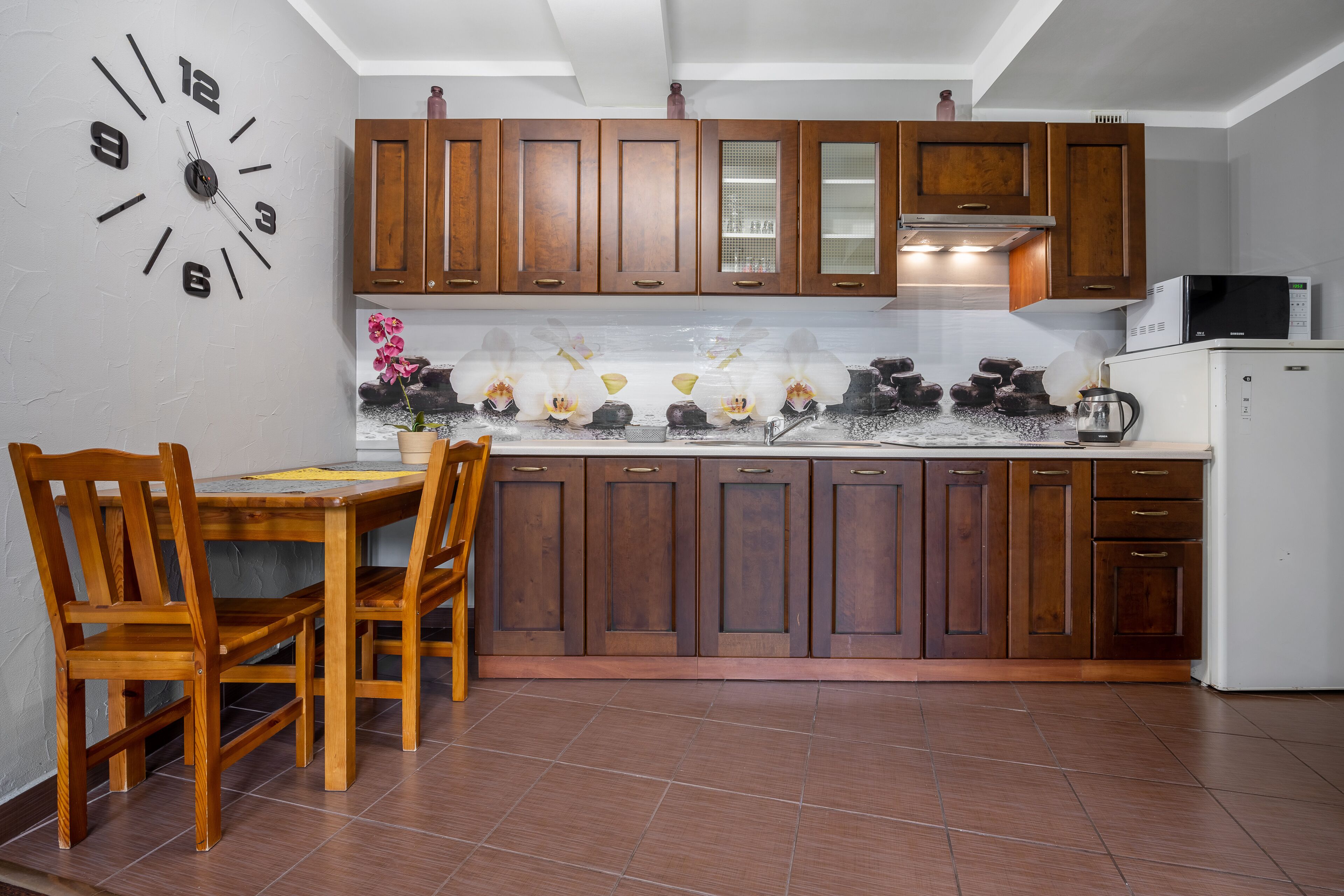 A kitchen with wooden cabinets, a clock, and a dining area with chairs.