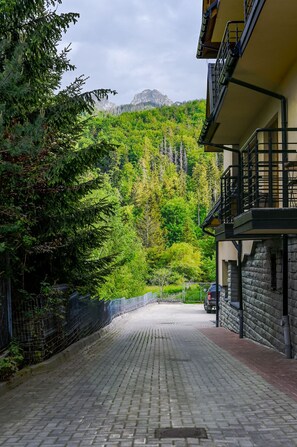 A paved driveway leading to a building with a stone facade, surrounded by lush greenery and a mountain in the background. - RentPlanet - Apartament Krzeptówki (Zakopane)
