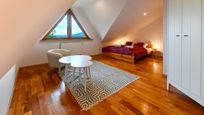 A bedroom with a sloped ceiling, a large window, a bed with red bedding, a white wardrobe, and a small table with two chairs. - RentPlanet - Apartament Krzeptówki (Zakopane)