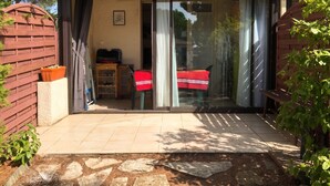 Una casa con puerta corrediza de vidrio, un pequeño armario de madera, una mesa cubierta con mantel rojo y una planta en maceta.