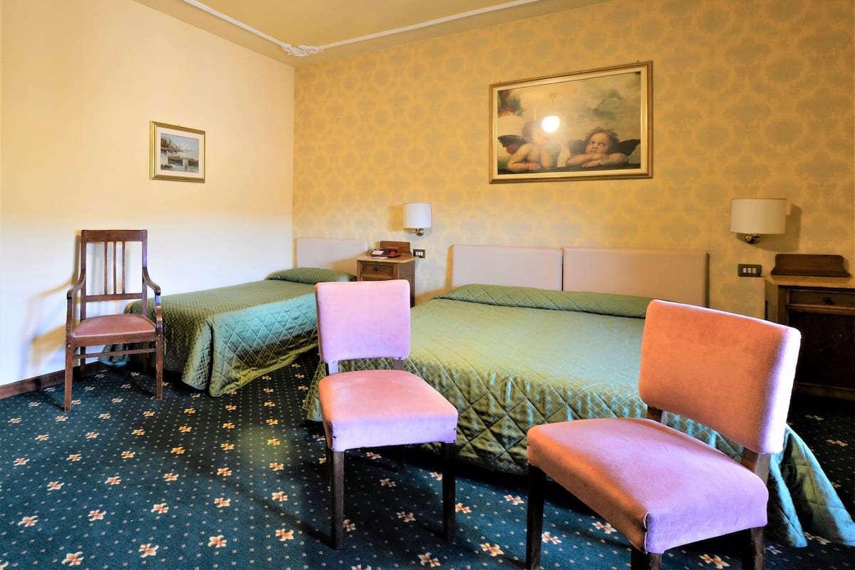 Una habitación de hotel con dos camas, una silla, una mesita de noche y un cuadro en la pared.