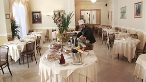 A formal dining room with multiple tables set for service, a chef preparing food, and a classic painting on the wall. - Grand Hotel Plaza e Locanda Maggiore (Montecatini Terme)