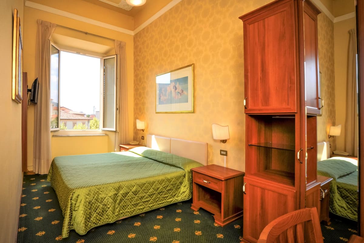Habitación de hotel con dos camas, un armario de madera, una mesita de noche con lámpara y un cuadro en la pared.