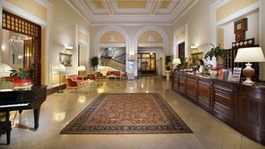 A spacious lobby with a grand piano, a large ornate rug, and a reception desk with a receptionist. - Grand Hotel Plaza e Locanda Maggiore (Montecatini Terme)