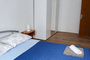 A bedroom with a bed, a nightstand, a lamp, a wardrobe, and a door.