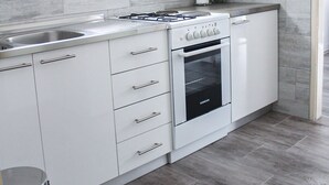 A modern kitchen with white cabinets, a gas stove, an oven, and grey tiled flooring. - Apartment Zvonimir (Kastela)