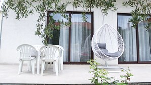 A patio with white plastic chairs, a white hanging chair, and olive trees. - Apartment Zvonimir (Kastela)