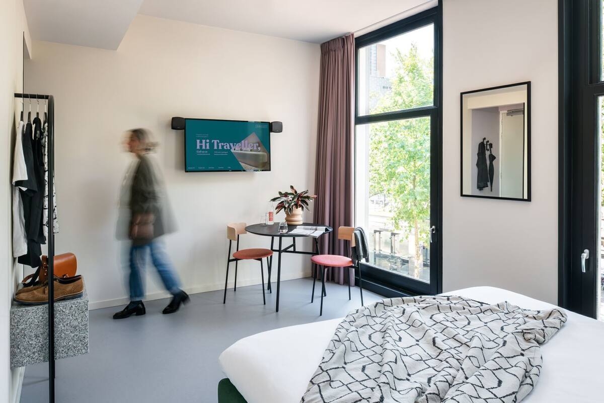 A hotel room with a bed, a table with chairs, a TV, and a window with curtains.