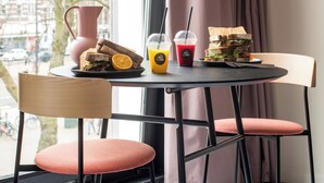 A dining area with a table set for two, featuring a sandwich, drinks, and a pitcher. - hotel emma next (Rotterdam)