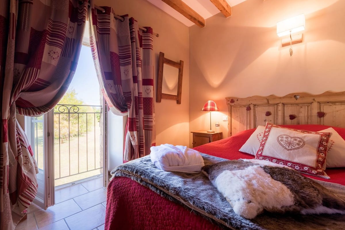A bedroom with a bed, a nightstand, a lamp, and a window with curtains.