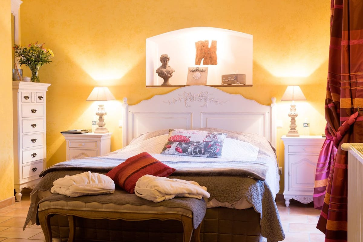 A neatly made bed with a pillow, a bedside table with a lamp, and a wall-mounted artwork above the bed.
