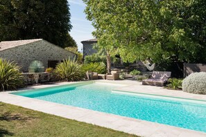 Relax by the serene pool surrounded by lush greenery and a rustic stone building.
