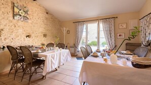 A dining area with a rustic stone wall, a table set for a meal, wicker chairs, and a view through the window.