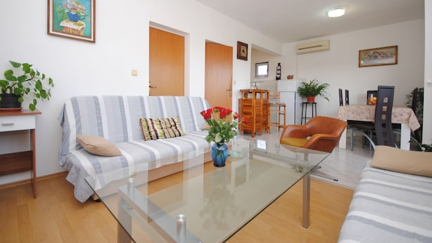 A living room with a sofa, a glass coffee table, a dining area with a table and chairs, and a kitchen in the background. - Apartment Ivanka (Kastela)
