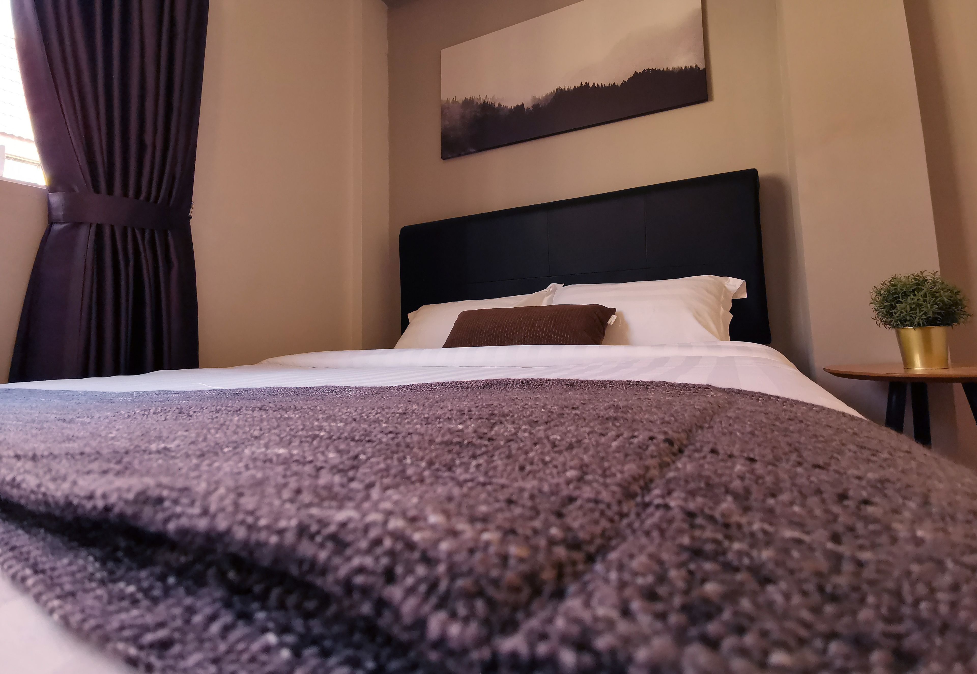 A neatly made bed with a dark headboard, white pillows, and a brown throw blanket.