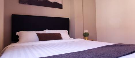 A neatly made bed with white and brown bedding, a dark headboard, and a small potted plant on a bedside table.