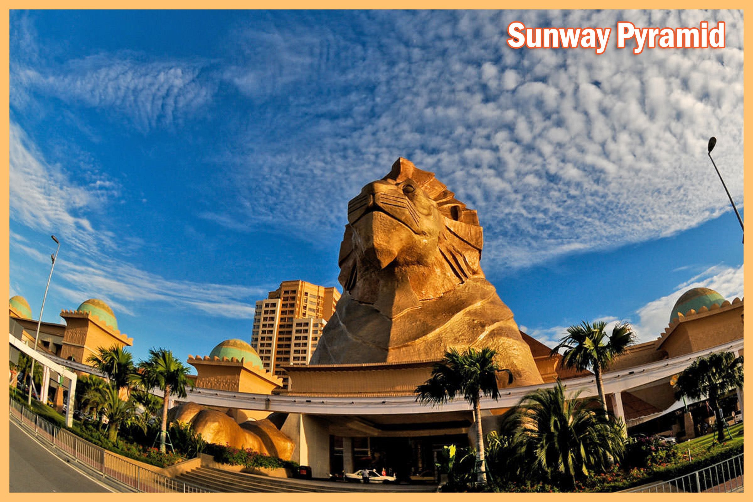 The Sunway Pyramid with a large stone lion statue, palm trees, and surrounding buildings.