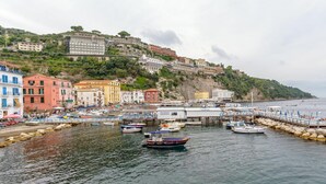 A coastal town with colorful buildings, a marina with boats, and a rocky hillside. - Caruso Sea View (Sorrento)