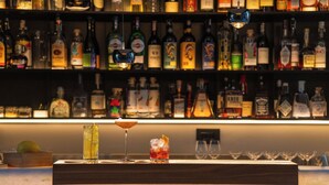 A bar area with a variety of liquor bottles on shelves and two glasses of cocktails on a wooden bar counter. - Caruso Sea View (Sorrento)