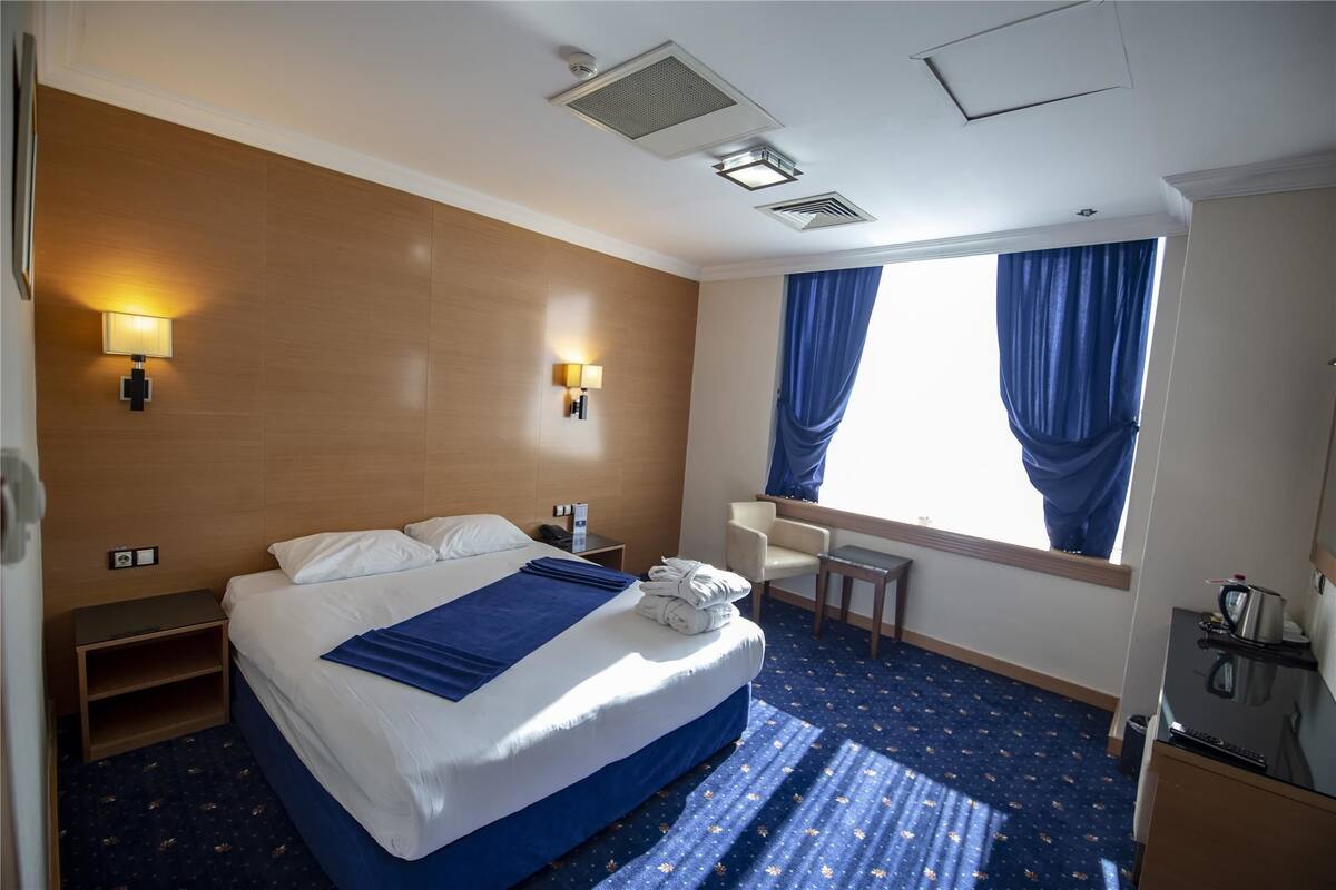 Ein Hotelzimmer mit Bett, Nachttischen, Schreibtisch, Stuhl und einem Fenster mit Vorhängen.