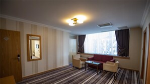 A hotel room with a striped carpet, a red sofa, two armchairs, a small table, and a large window with curtains. - Gaziantep Plaza Hotel (Gaziantep)