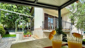 Una mesa con dos vasos de jugo de naranja, una bandeja y vistas de una casa con balcón y plantas en macetas.