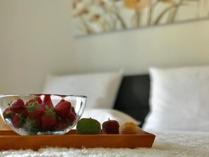 A bowl of strawberries on a tray with a bed and pillows in the background. - Apartment Adri (Rovinj)