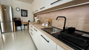 Una cocina moderna con un refrigerador de acero inoxidable, una encimera de madera, un lavamanos negro y una cafetera.