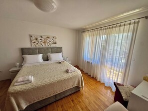 Un dormitorio con cama, mesita de noche, cortinas y una obra de arte en la pared.