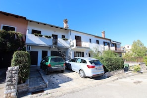 A row of two-story houses with a central staircase, parked cars, and a clear blue sky.