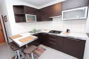 A modern kitchen with dark brown cabinets, a white countertop, a stainless steel sink, and a gas stove.