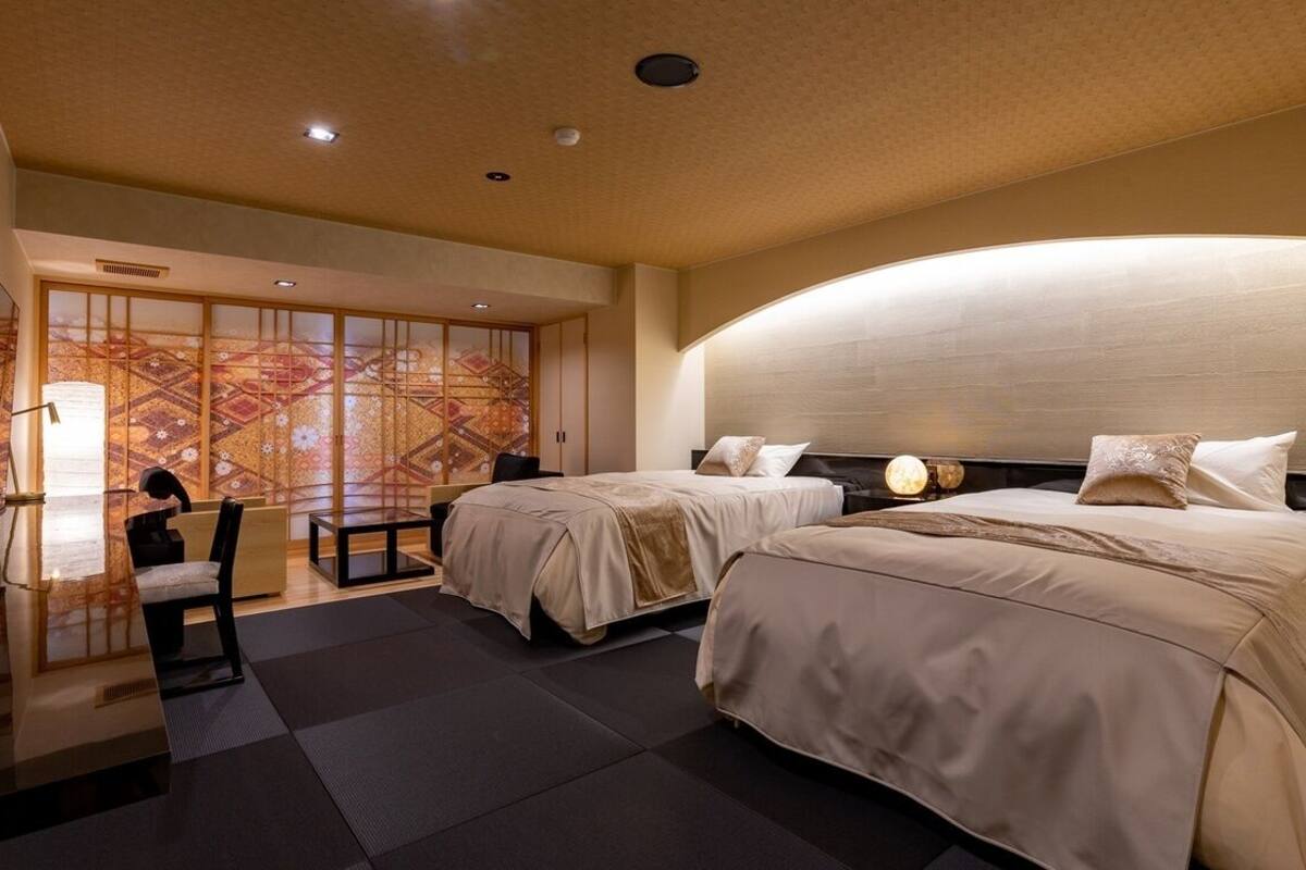 A hotel room with two beds, a desk, and a traditional Japanese sliding door.