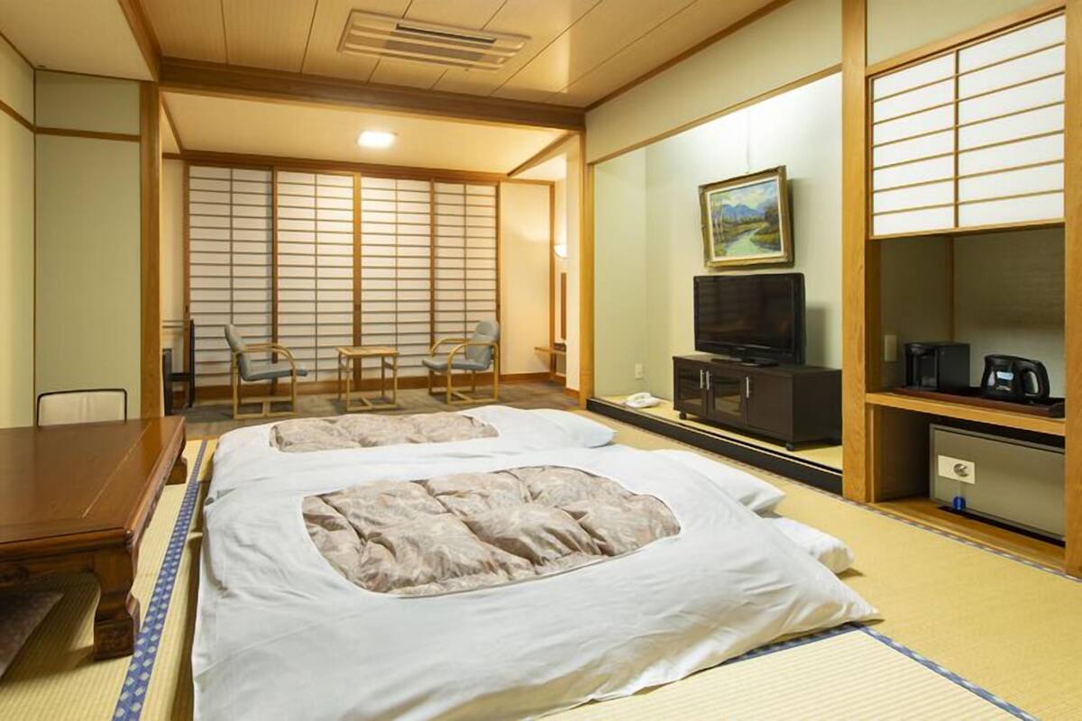 A traditional Japanese-style hotel room with tatami flooring, a bed with a futon, a television, and a small cabinet.