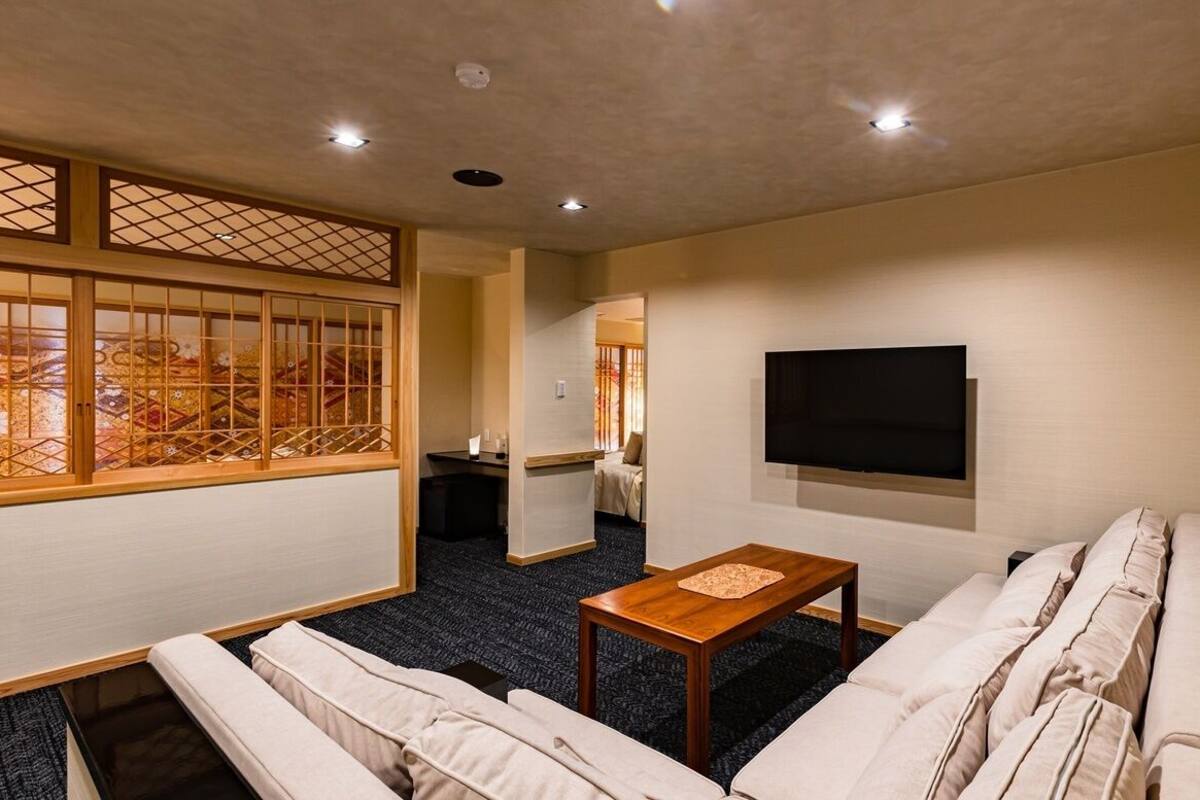 A living room with a sofa, a coffee table, a TV mounted on the wall, and a traditional Japanese sliding door.