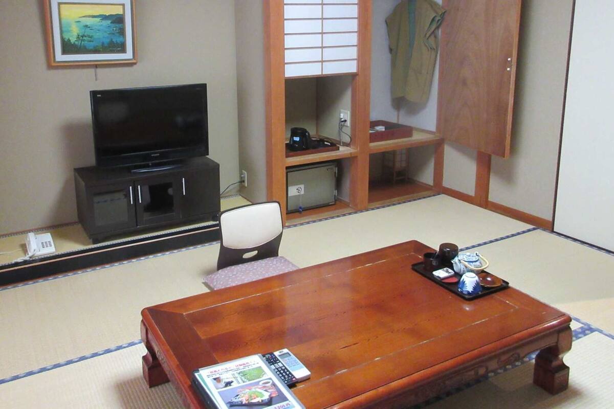 A traditional Japanese room with tatami flooring, a television on a cabinet, a wooden table with a tray, and a sliding door closet.