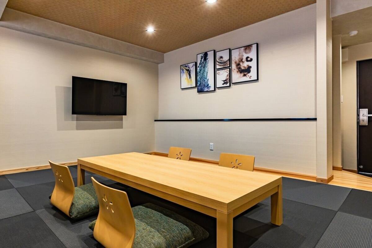 A conference room with a long table, four chairs, a flat-screen TV, and abstract art on the wall.