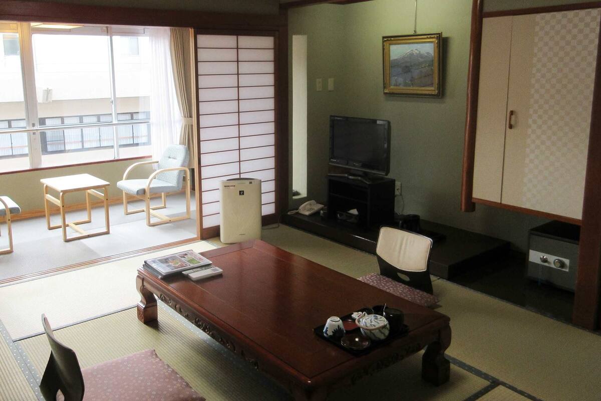 A traditional Japanese-style room with tatami flooring, a low table, a sofa, a television, and a cabinet.