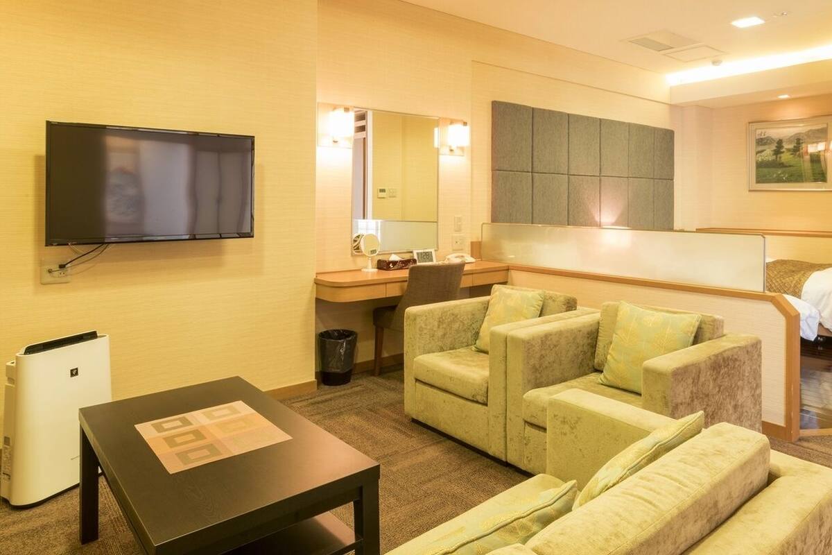 A hotel room with a flat-screen TV, a desk with a chair, a sofa, and a bed.