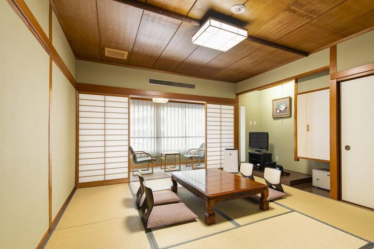 A traditional Japanese-style room with tatami flooring, a low table, chairs, a television, and sliding doors.