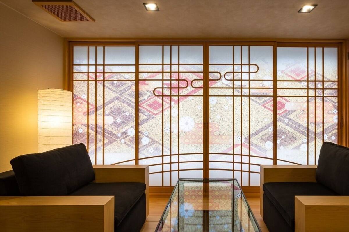 A room with a traditional sliding door, two black sofas, a glass coffee table, and a lamp.