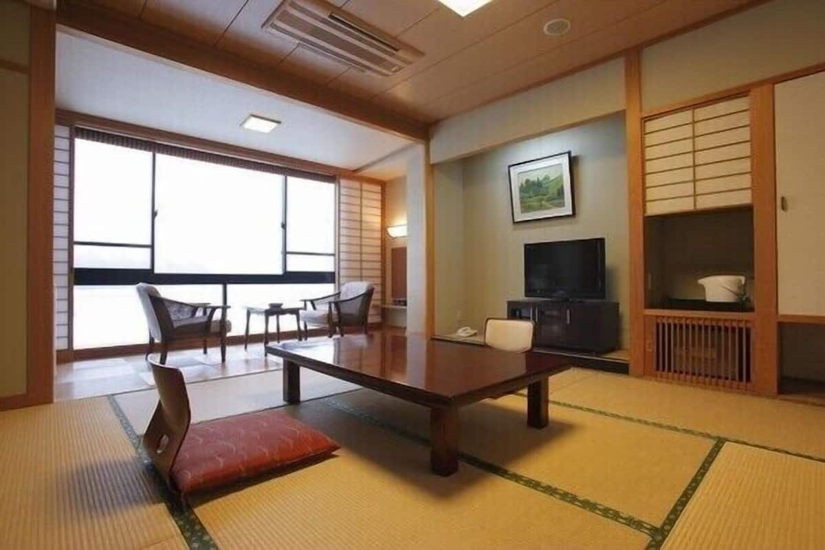 A traditional Japanese room with tatami flooring, a low table, chairs, a television, and a sliding door.