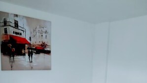 A hotel room with a bed, white bedding, and a painting of a city scene. - Walter Place (Edgware)